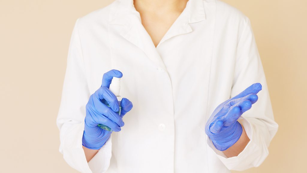 crop-medical-worker-spraying-sanitizer-over-hands-in-gloves-4492050